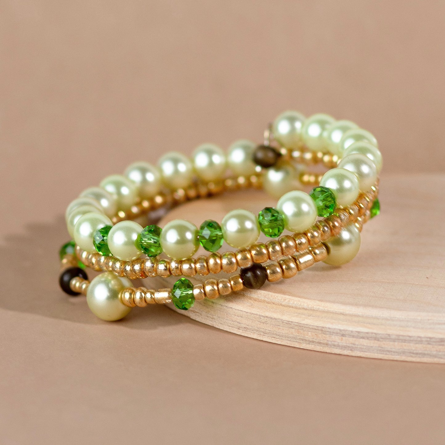 Beaded bracelet with pearls, green stones, and gold accents on a beige background