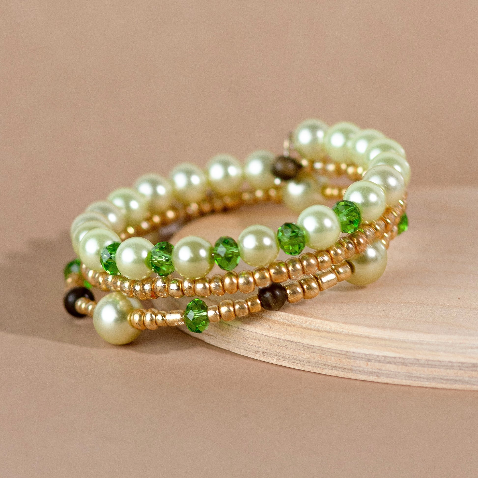 Beaded bracelet with pearls, green stones, and gold accents on a beige background